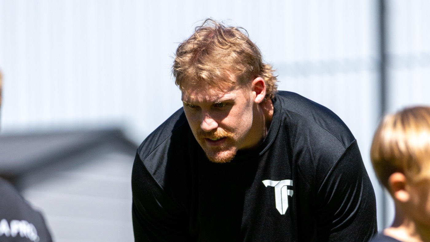 A Triple F coach crouches beside two young players, teaching during practice.
