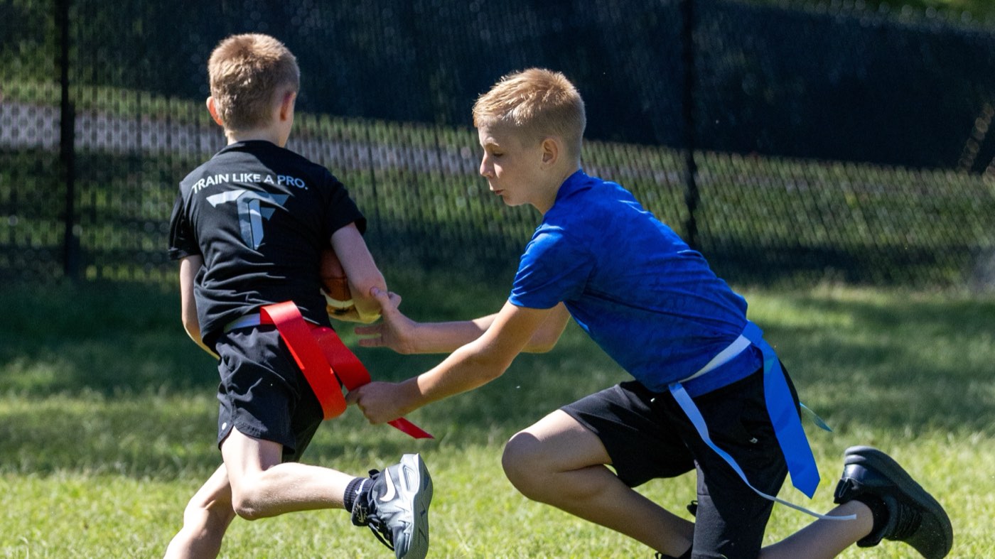 A defender pulls the flag from a ball carrier in full stride on a grass field.